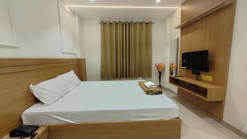 Una habitación de hotel con una cama de madera, un televisor en un estante de madera, una cortina y una pequeña mesa con un florero.