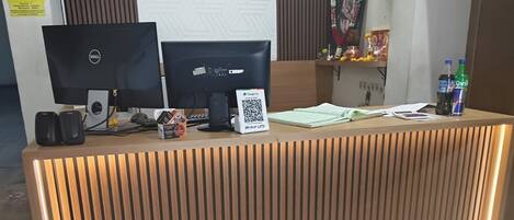 A reception desk with two monitors, a QR code, a phone, and a small speaker.