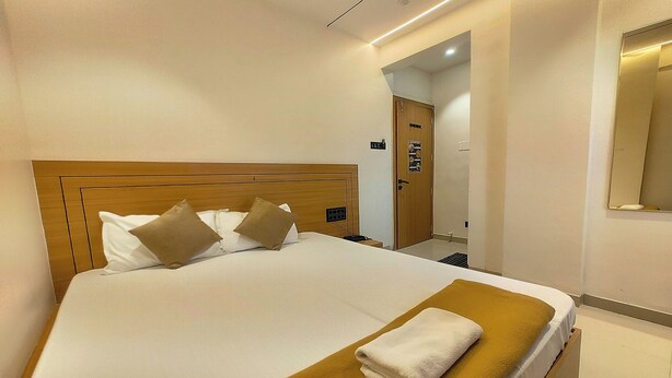 Une chambre d’hôtel avec un lit, une tête de lit en bois, un plaid marron et une serviette blanche.