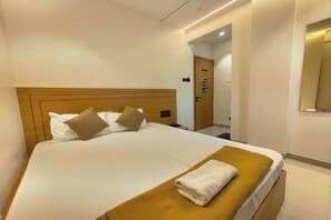 A hotel room with a bed, a wooden headboard, a brown throw blanket, and a white towel. - Sai Pavilion Lodging (Pune)