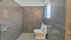 Une salle de bain avec douche, toilettes et lavabo, le tout adossé à des murs en marbre.