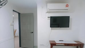 A room with a closed door, an air conditioner, a mounted flat-screen TV, and a small wooden table. - Confidence Motel (Langkawi)