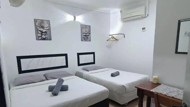 A small, clean room with two beds, a fan, a table with a bottle, and a wall-mounted air conditioner. - Confidence Motel (Langkawi)