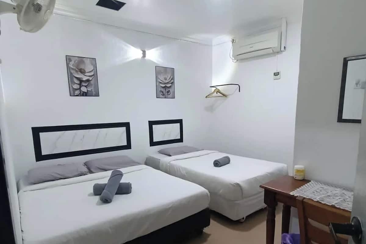 A small, clean room with two beds, a fan, a table with a bottle, and a wall-mounted air conditioner.