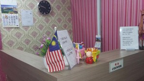 A hotel reception desk with a clock, a calendar, a flag, and a sign indicating check-in times. - Confidence Motel (Langkawi)