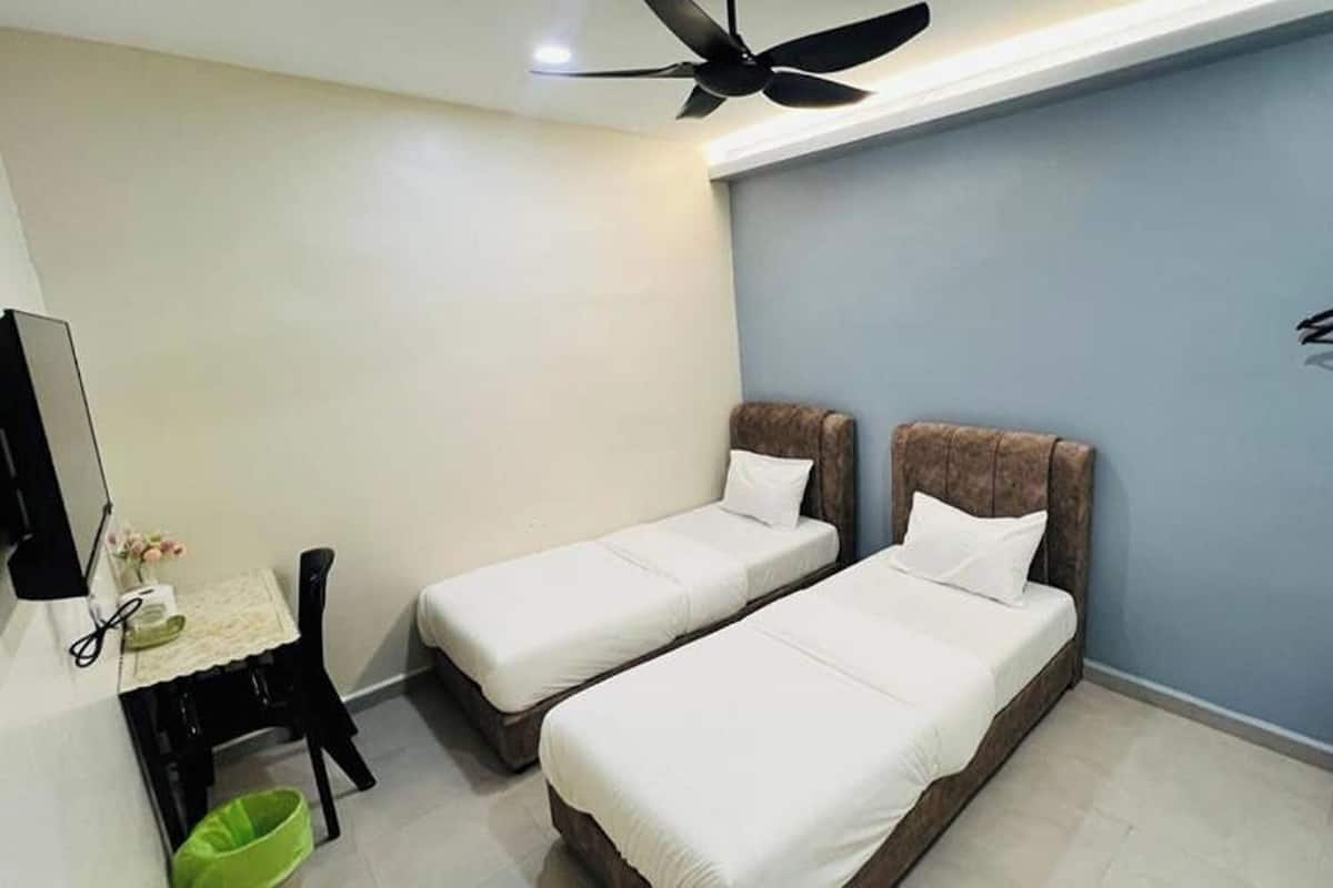 A small room with two single beds, a desk with a chair, a green trash bin, and a ceiling fan.