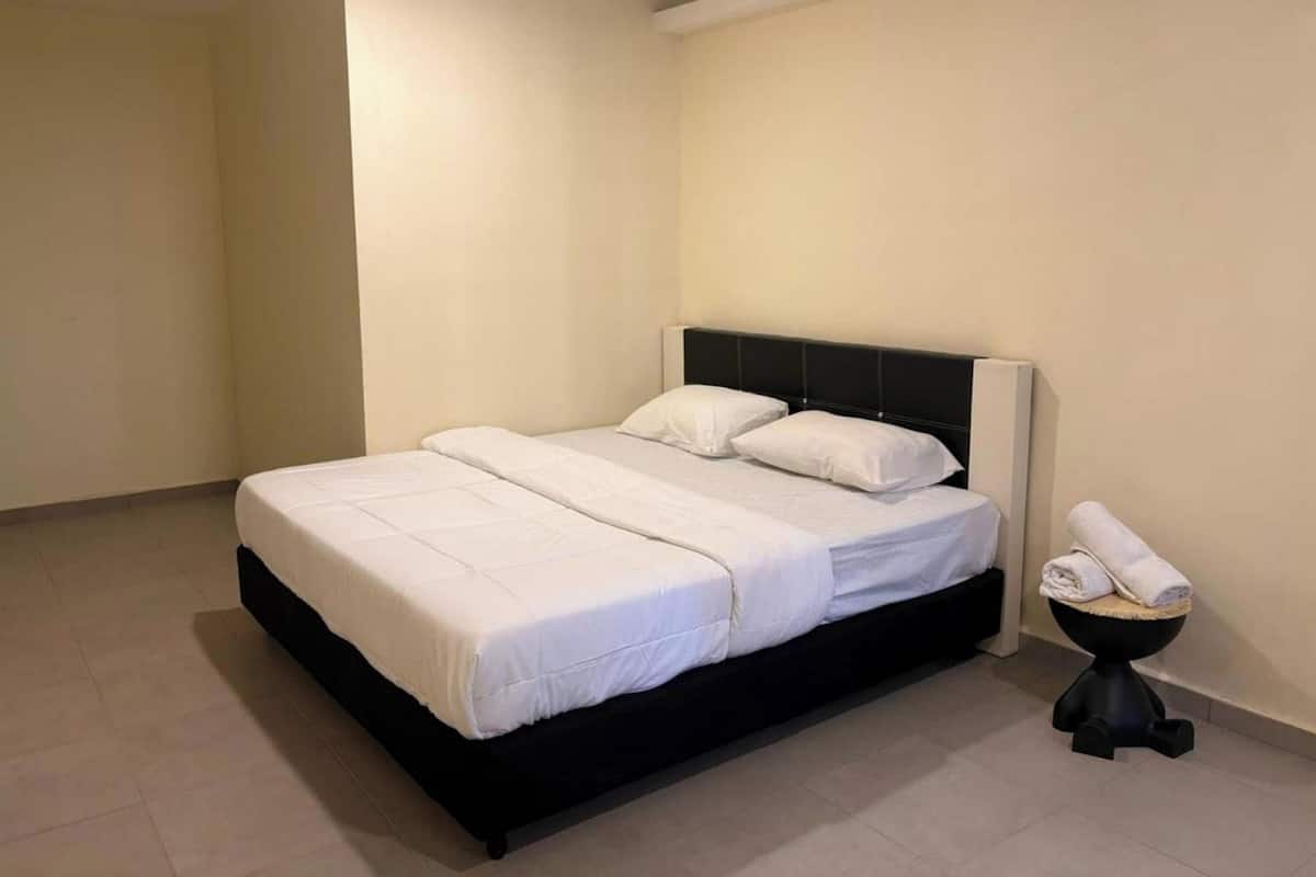A neatly made bed with white linens in a simple room with plain walls and a tiled floor.