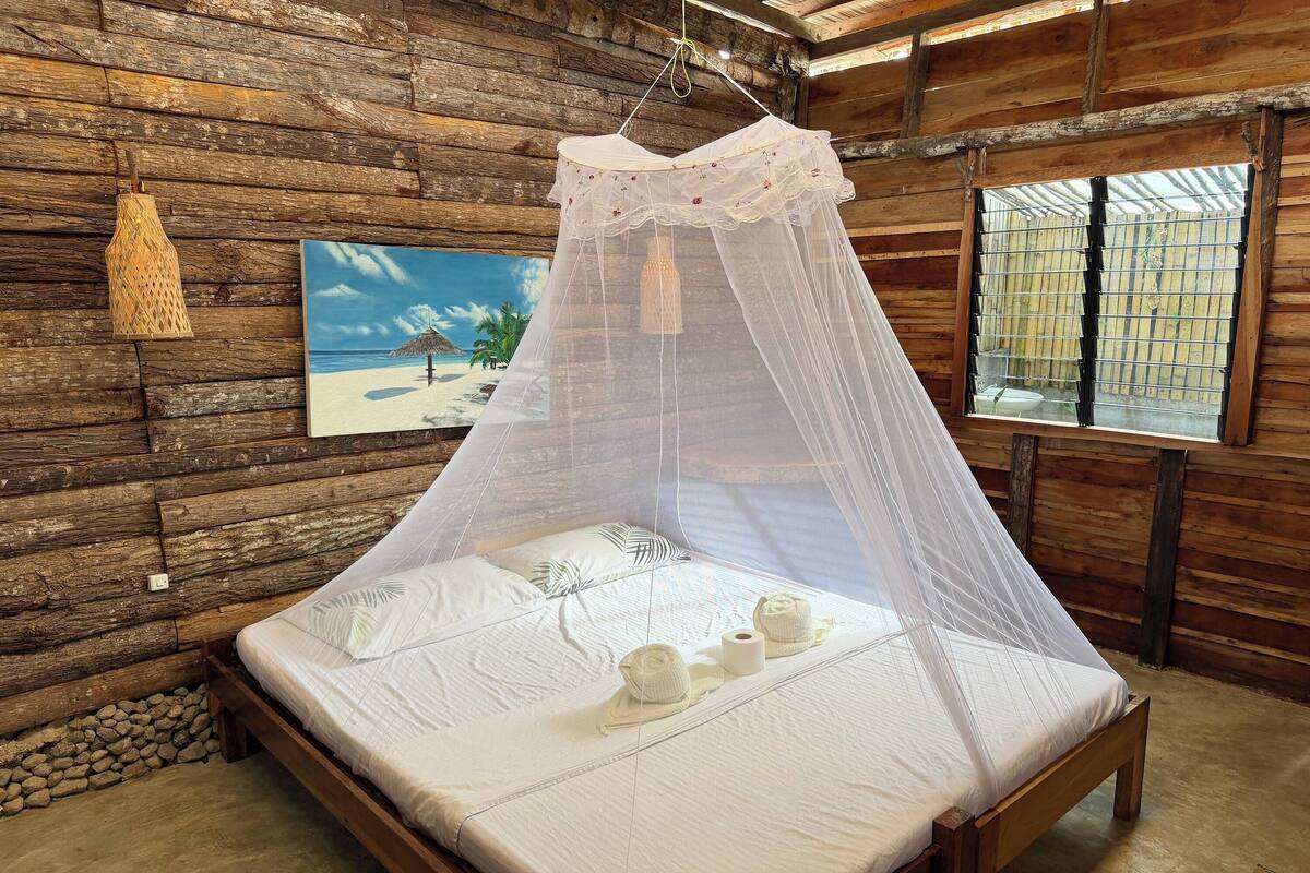 Habitación de cabaña de madera con cama, un cuadro y un mosquitero.