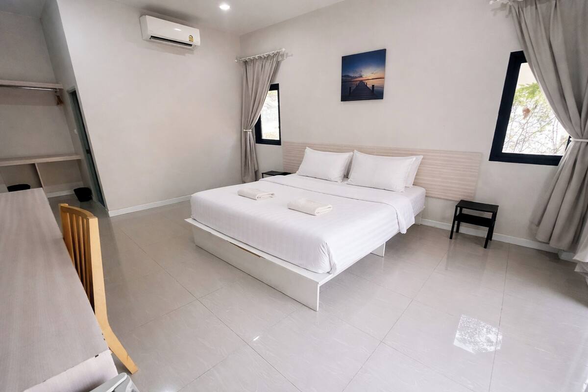 A modern bedroom with a large bed, a small bedside table, and a window with curtains.