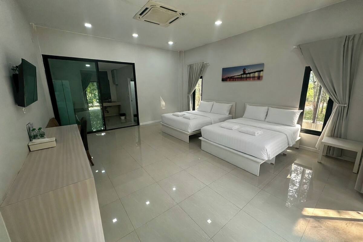 A modern hotel room with two beds, a large mirror, a flat-screen TV, and a sliding glass door leading to a balcony.