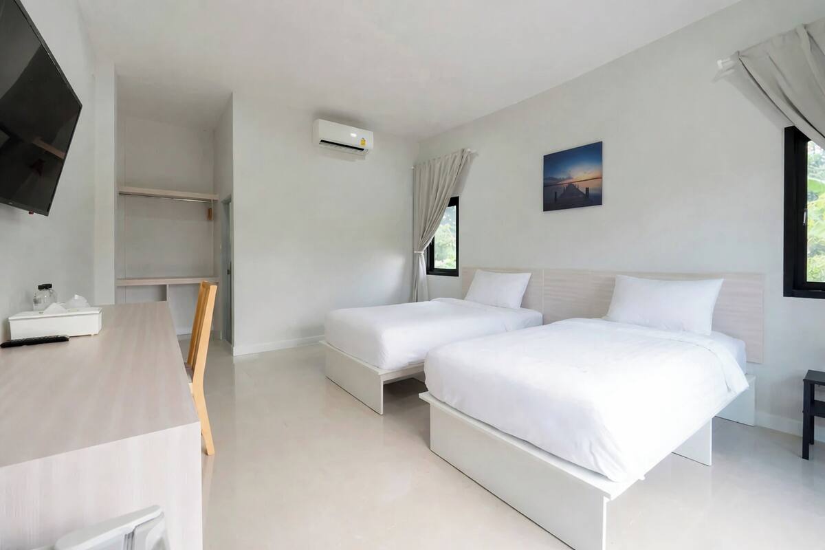 A modern hotel room with two beds, a desk, and a TV.
