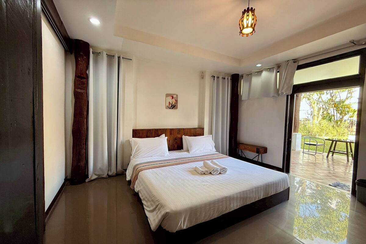 A hotel room with a large bed, a wooden headboard, a small table, and a view of the outdoors.