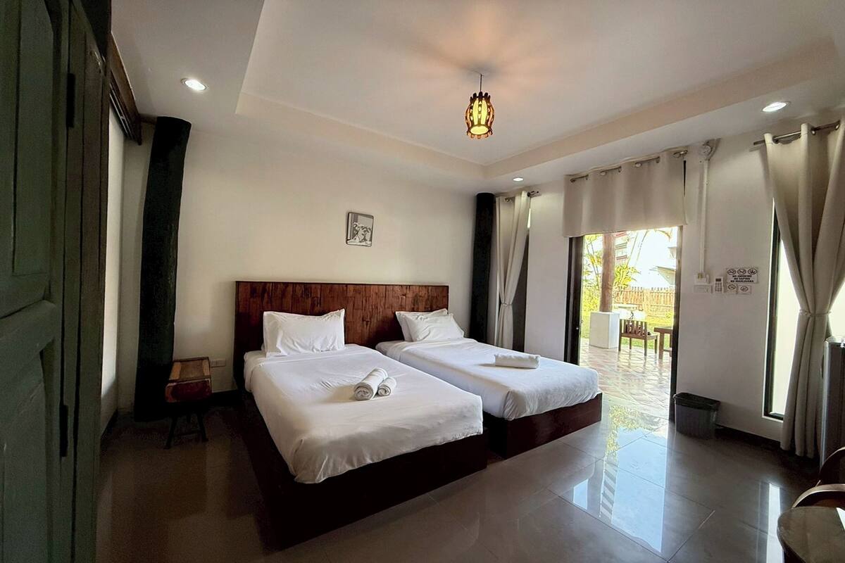 A hotel room with two beds, a wooden headboard, a ceiling light, and a view of the outside.