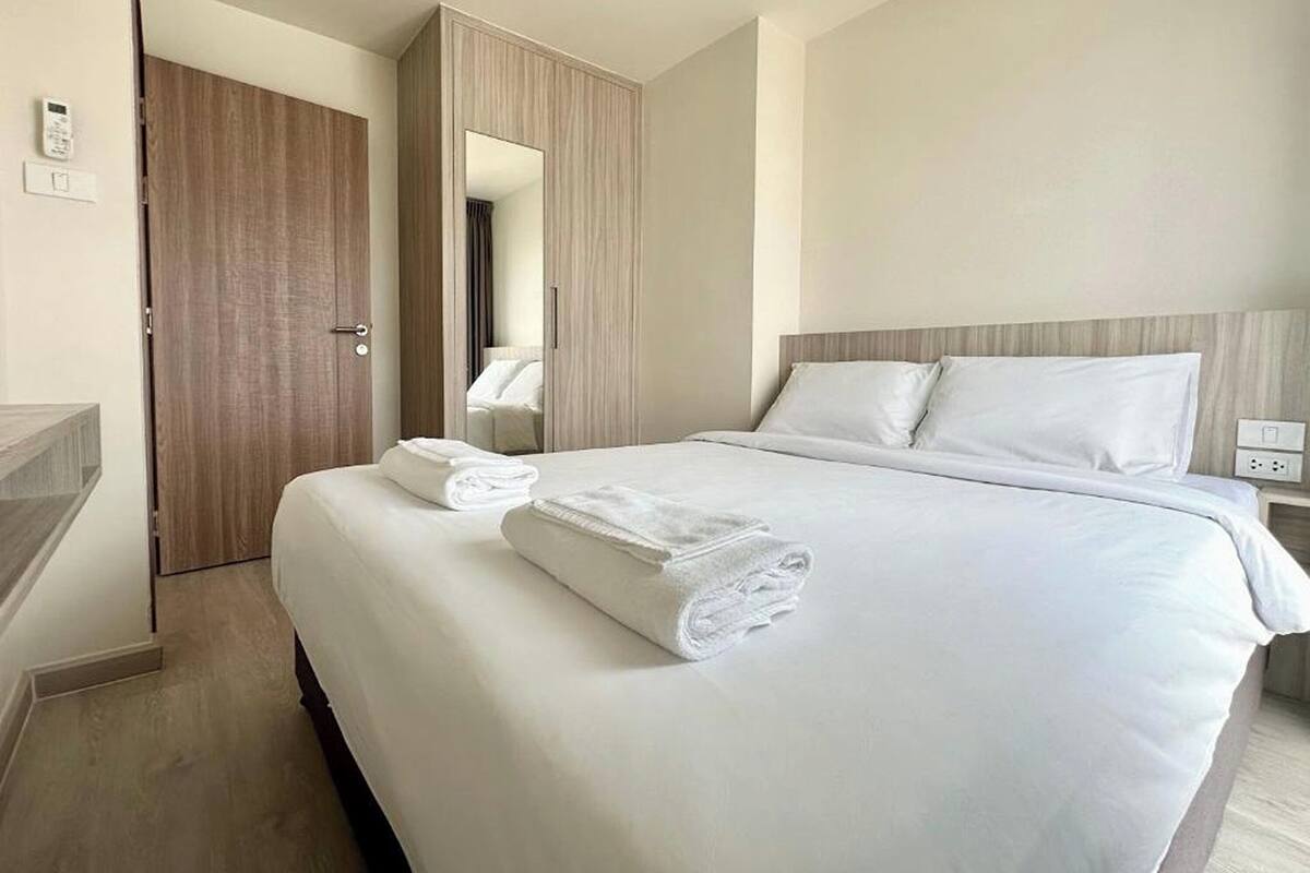 A hotel room with a large bed, a wooden door, a mirror, and a bedside table.