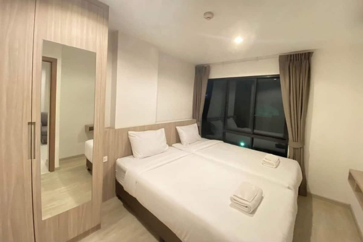 A hotel room with a large bed, a wardrobe, a window with curtains, and a mirror.