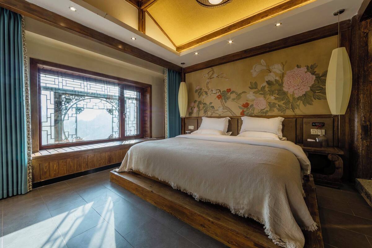 A bedroom with a large bed, wooden headboard, a window with traditional lattice design, and a wall mural.