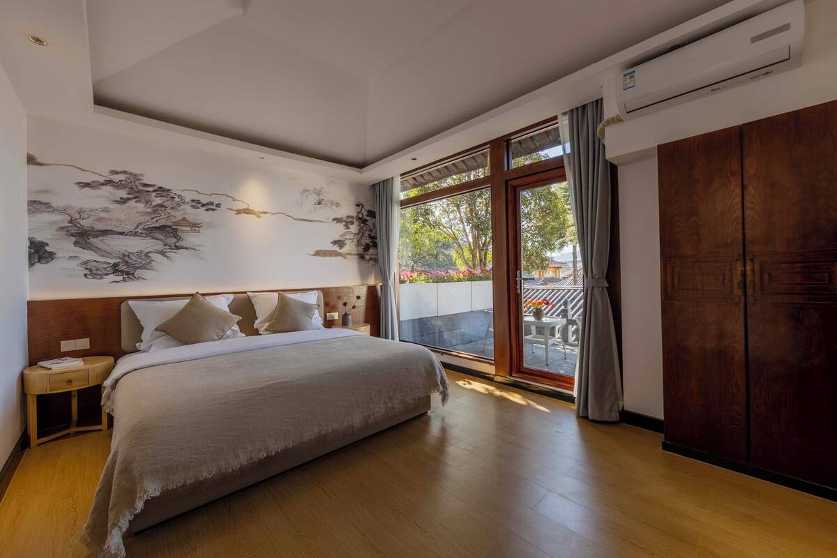 A bedroom with a large bed, a nightstand, a wall mural, and a sliding glass door to an outdoor area.