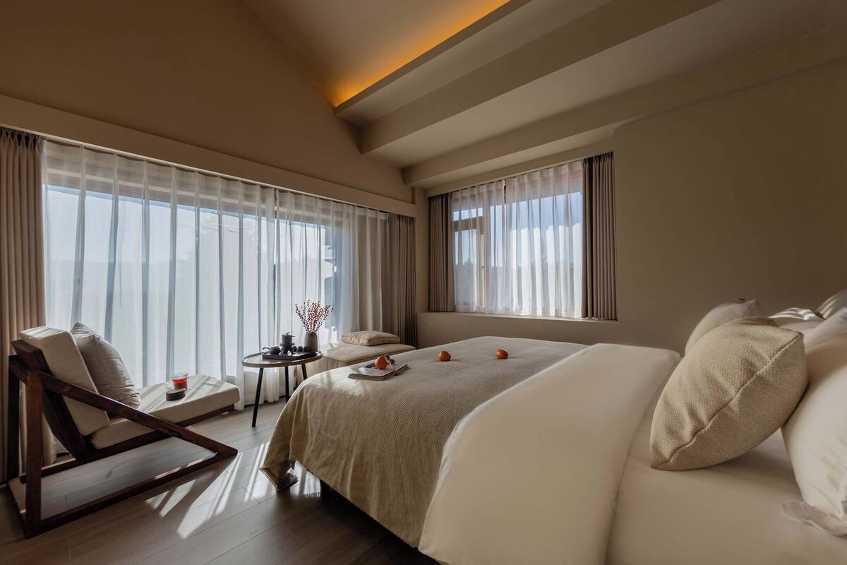 A hotel room with a large bed, a sofa, a small table with a drink, and sheer curtains.