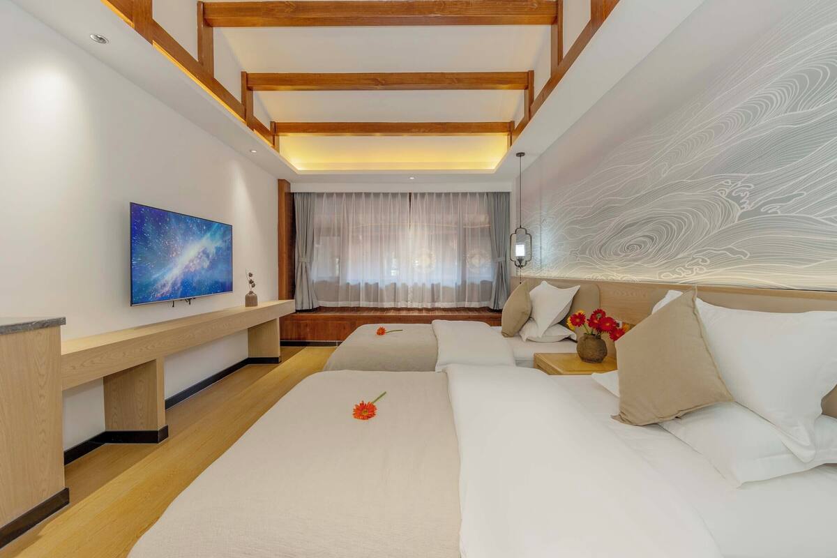 A hotel room with a bed, a TV, a desk, and a window with curtains.