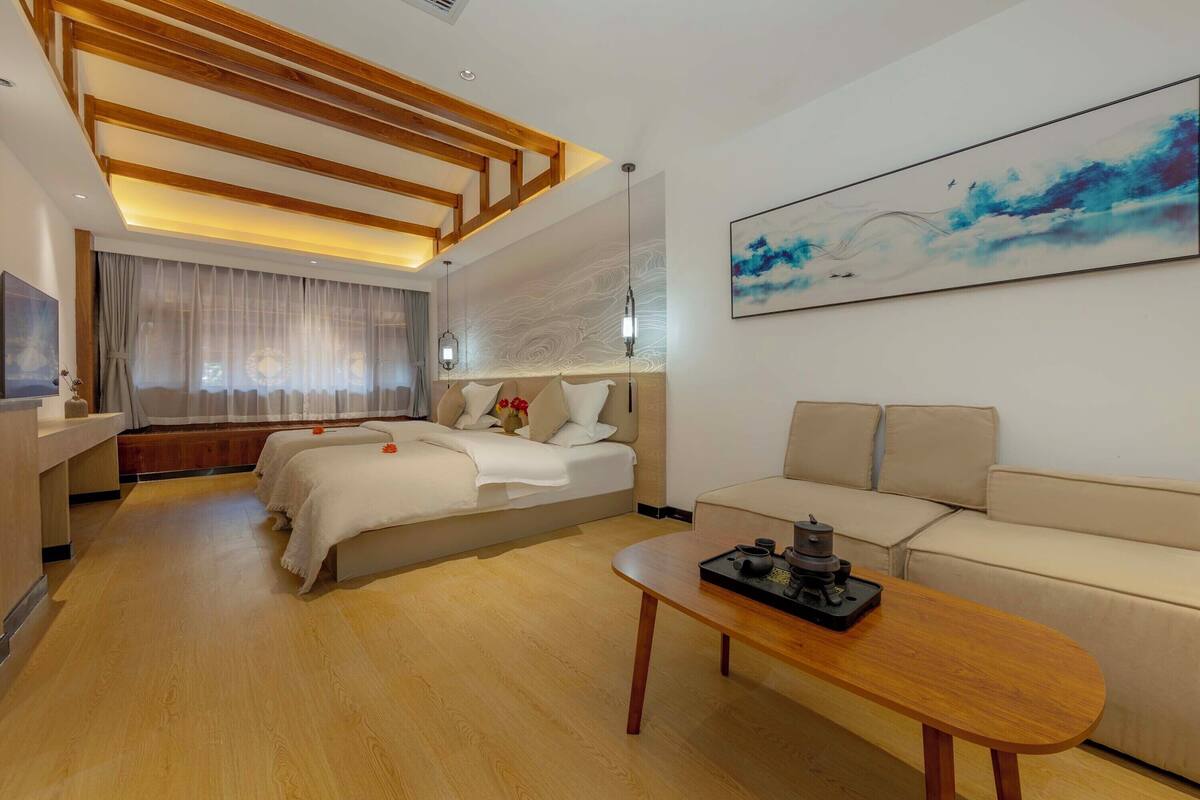 A modern hotel room with a wooden ceiling, a large bed, a sofa, a coffee table, and a painting on the wall.