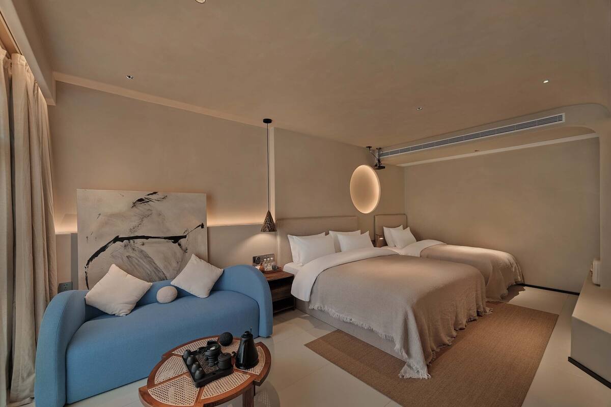 A modern hotel room with a large bed, a smaller sofa, a coffee table, and a painting on the wall.