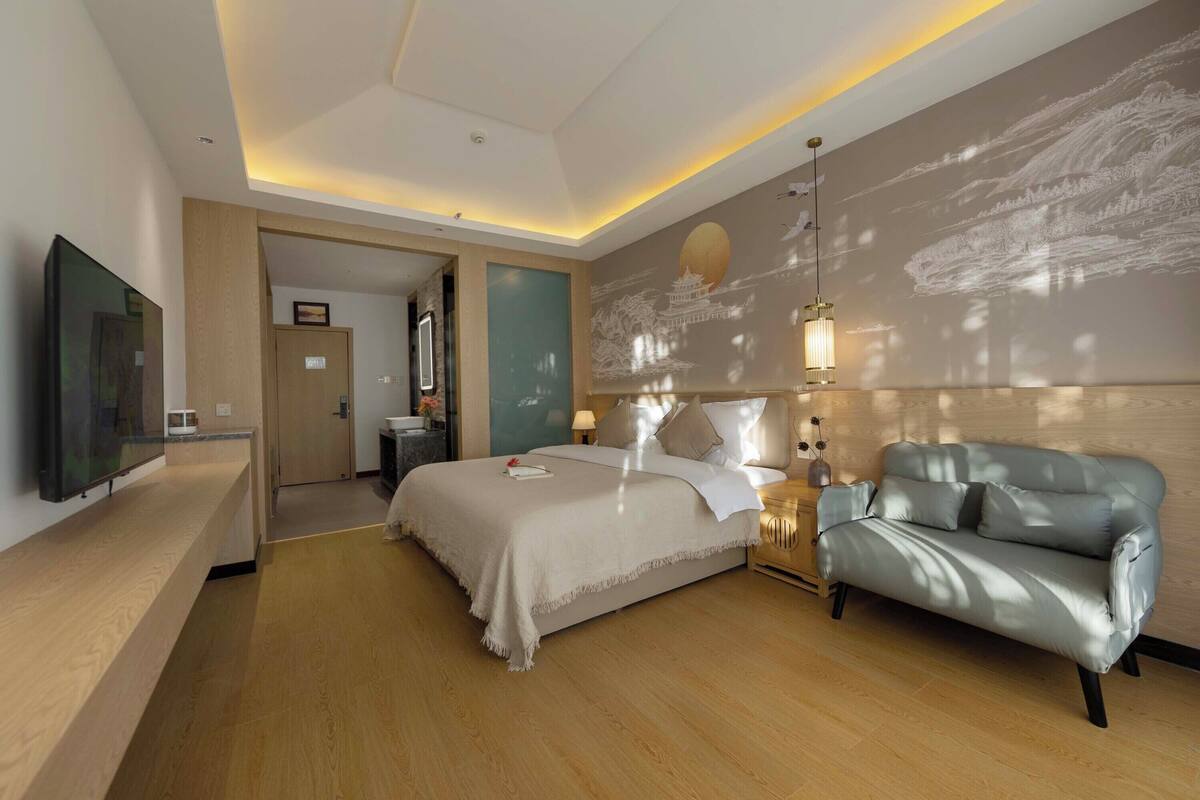 A modern hotel room with a large bed, a sofa, a flat-screen TV, and a wall with a mural.