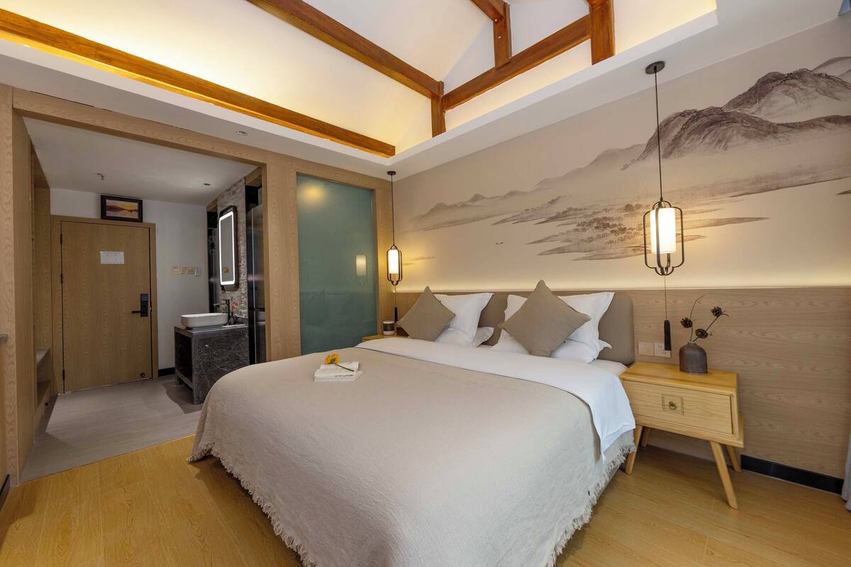 A bedroom with a large bed, wooden headboard, bedside table, and a wall-mounted lamp.