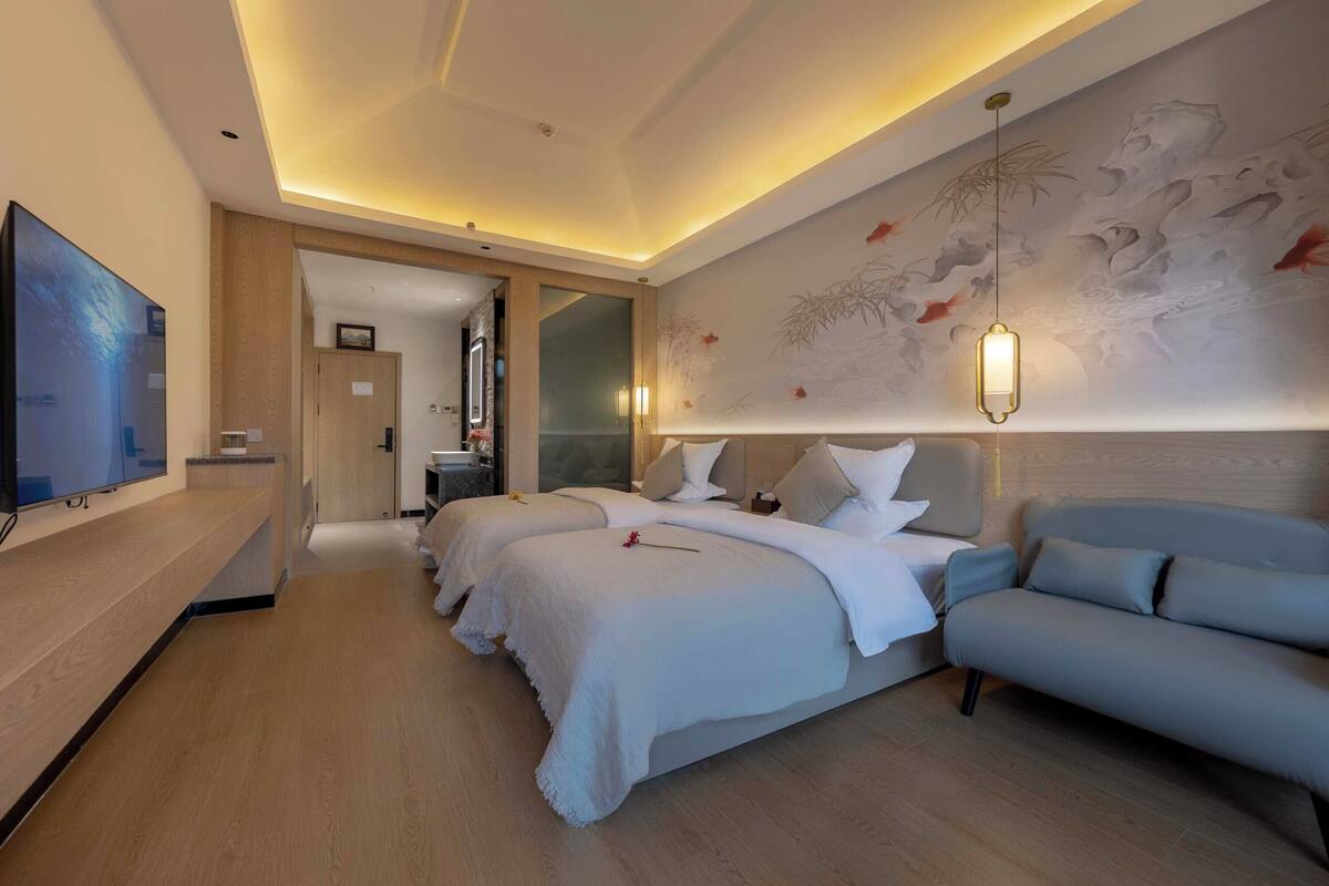 A hotel room with a large bed, a sofa, a TV, and a wall with a mural.