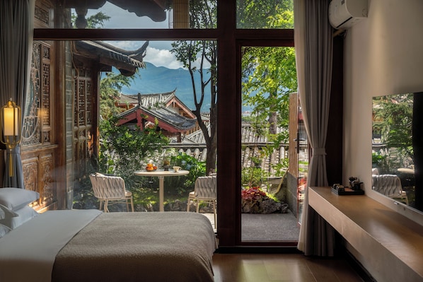 A hotel room with a traditional Chinese architectural view through a glass door, a bed, a small table with fruit, and a seating area with chairs.