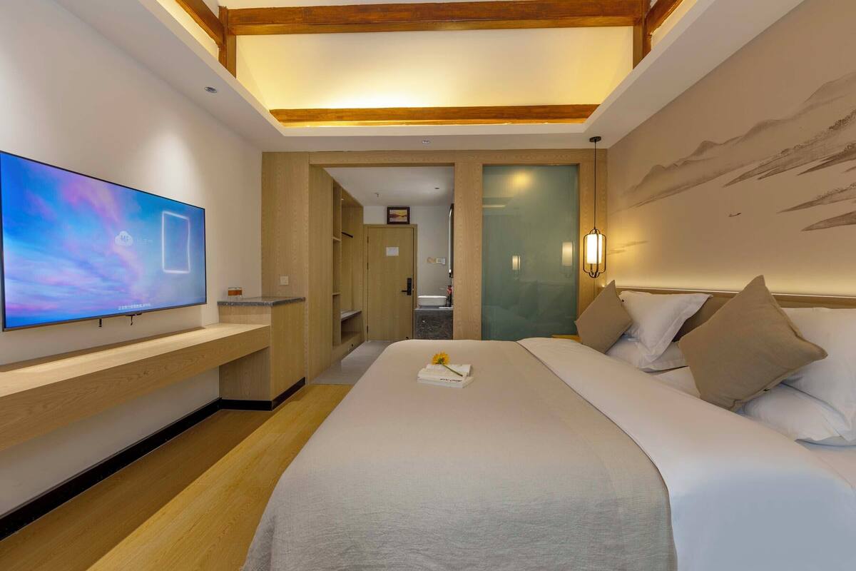 A modern hotel room with a large bed, a flat-screen TV, wooden flooring, and a painting on the wall.