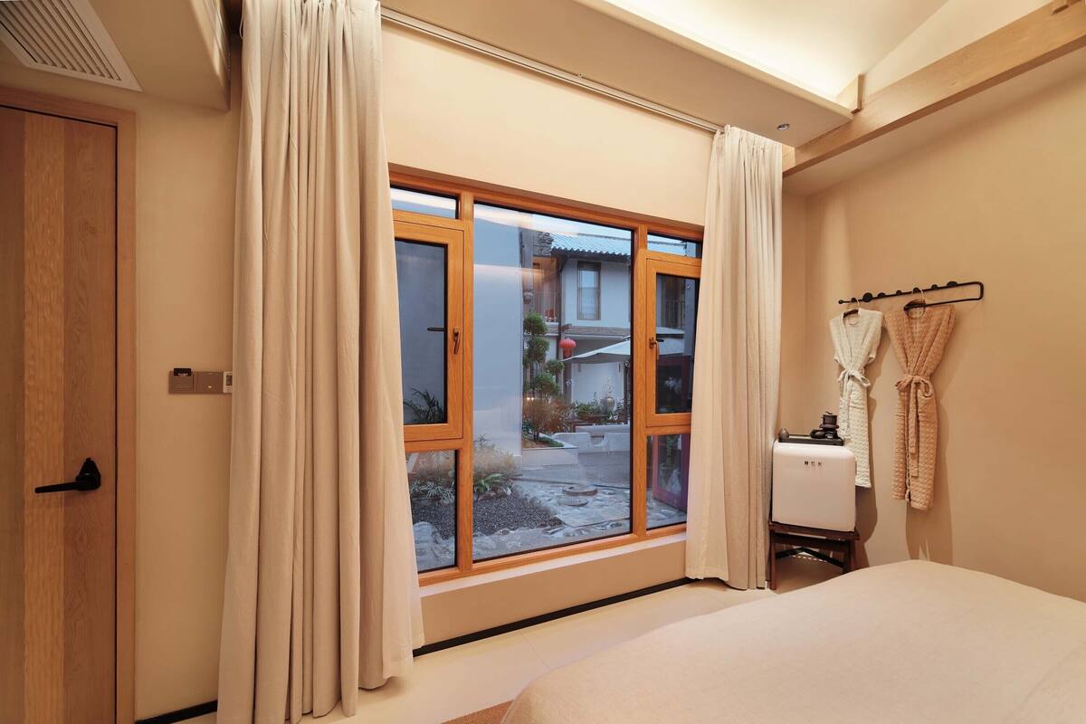 A hotel room with a large sliding glass door to the outside, a bed, a small bedside table, and a wall-mounted robe rack.