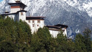 A traditional building with multiple levels and a prominent tower, surrounded by snow-covered mountains and dense forest. - Haven Resort and Spa (Paro)