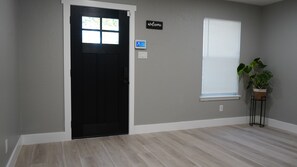 Ein Zimmer mit einer schwarzen Tür, einem 'Welcome'-Schild, einem Thermostat und einem Fenster mit Jalousien.