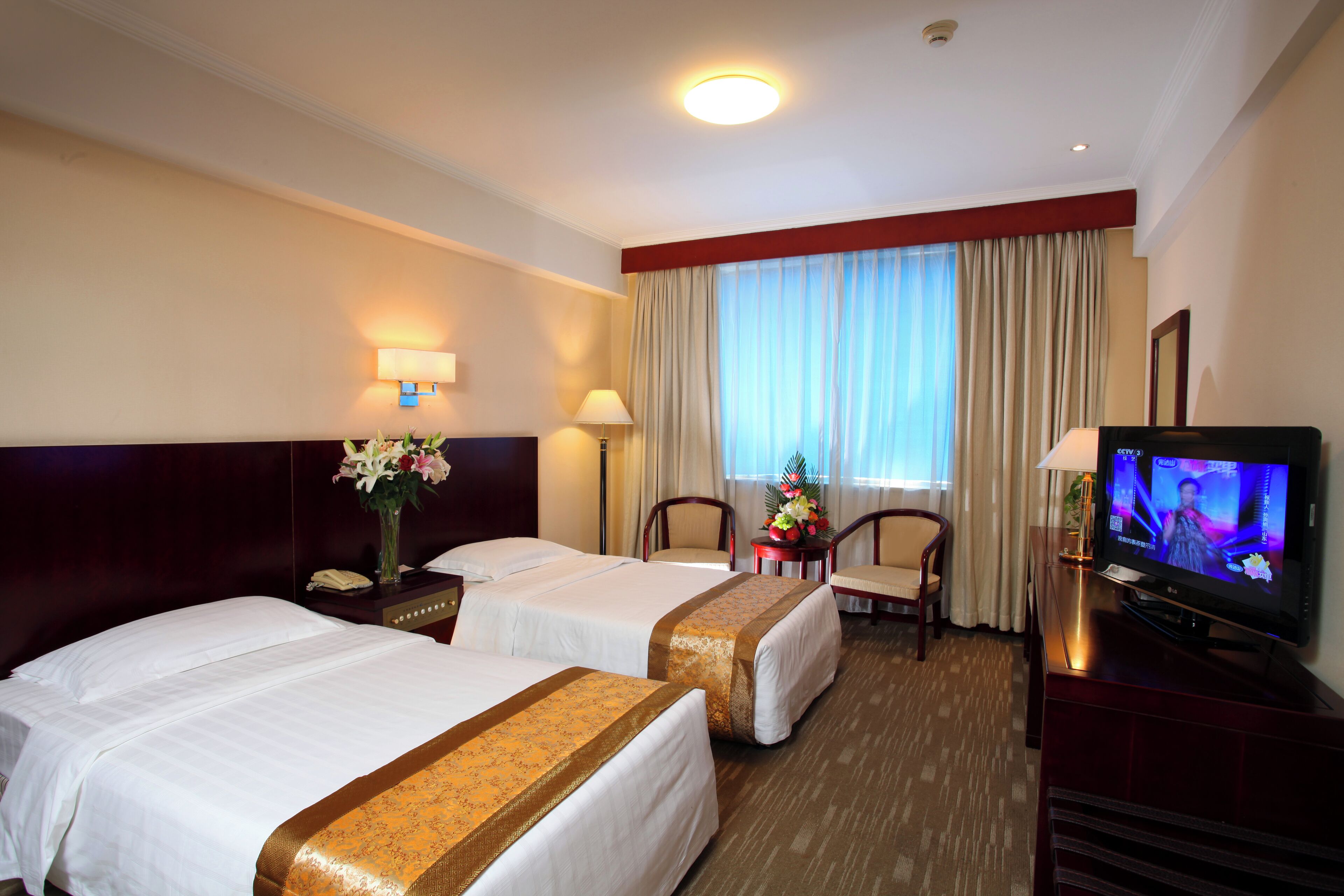Habitación de hotel con dos camas, televisión, escritorio con lámpara y ventana con cortinas.