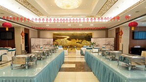 A banquet hall with long tables covered in blue tablecloths, equipped with buffet stations.