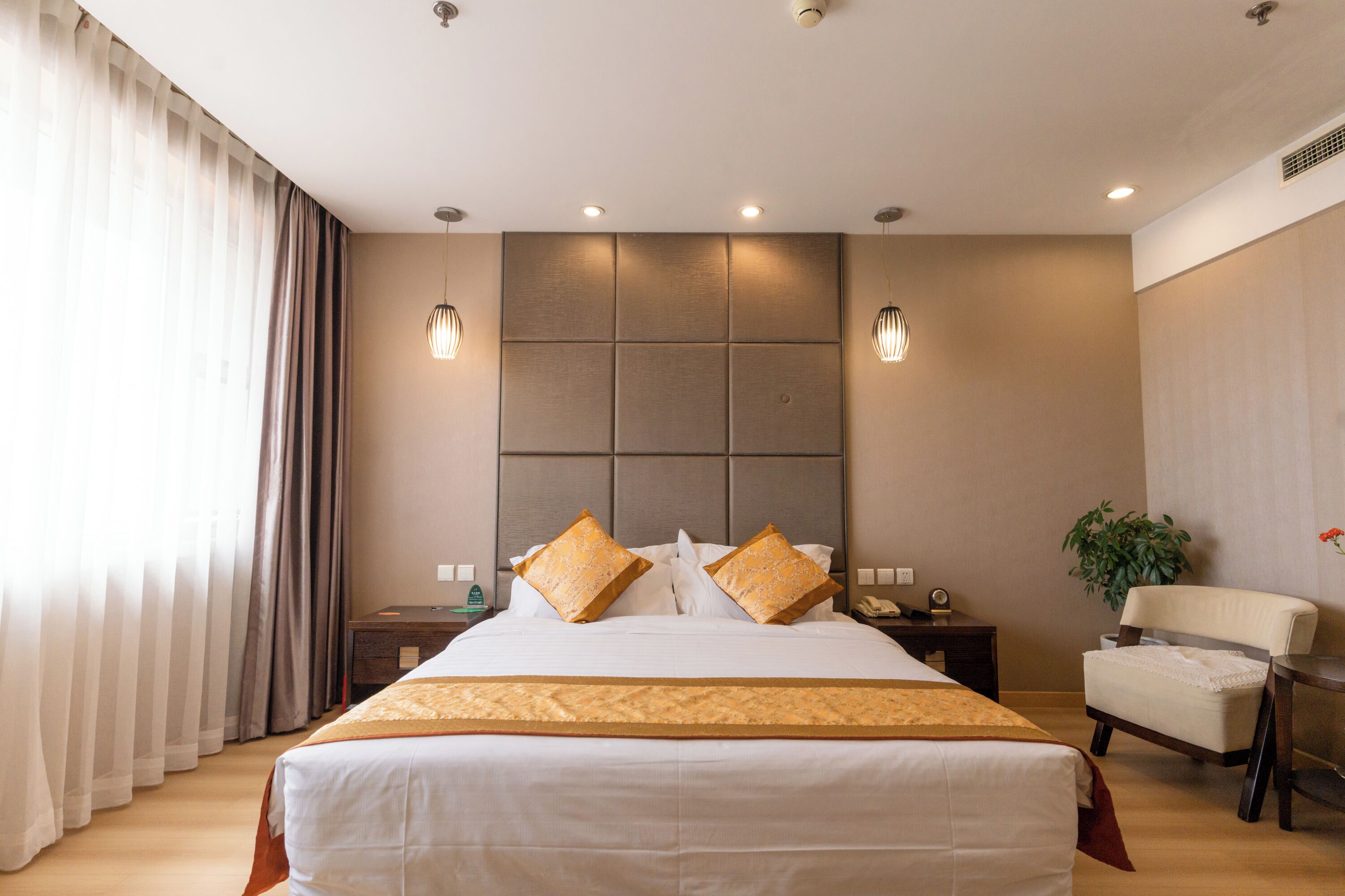 A hotel room with a large bed, a desk, a chair, and a potted plant.