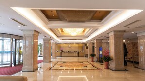 A spacious lobby with a reception desk, a large chandelier, and a red carpet leading to the entrance.
