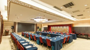 A conference room with long tables, red chairs, and a large screen.