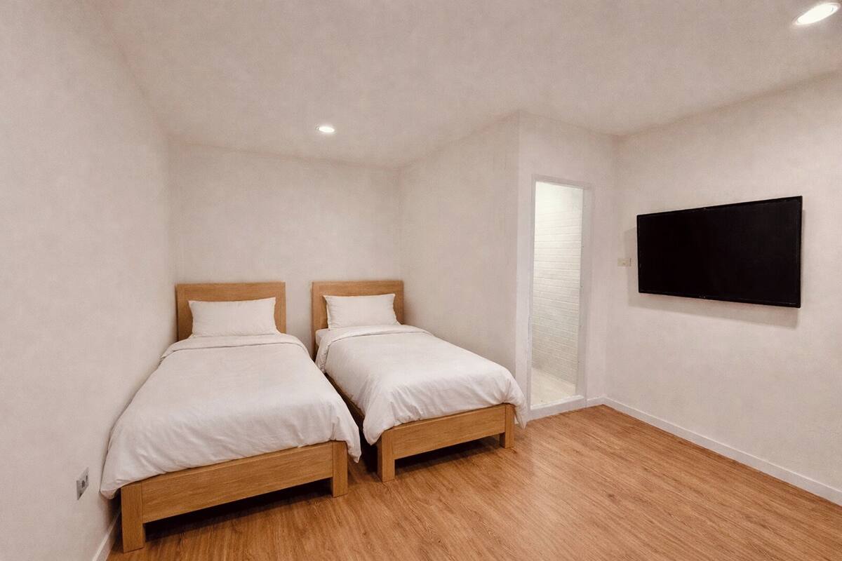 A room with two wooden beds, a flat-screen TV mounted on the wall, and a wooden floor.