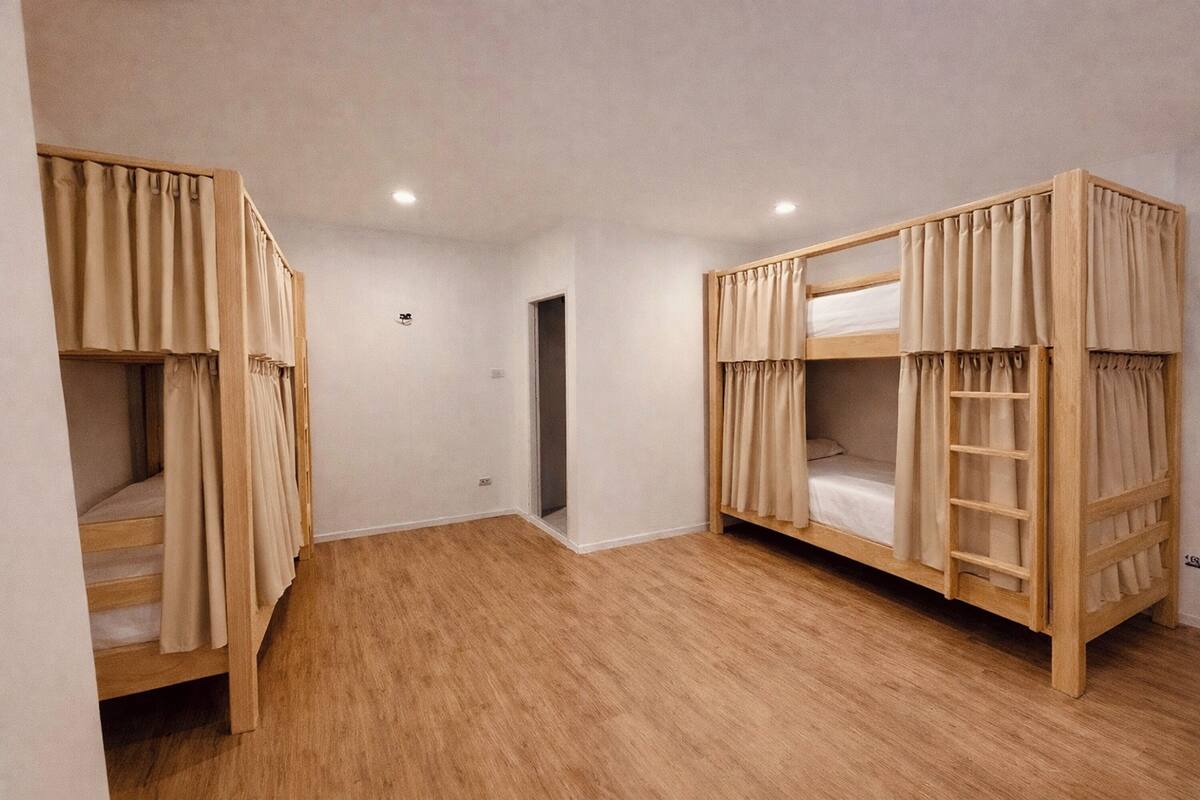 A room with two bunk beds, wooden flooring, and a door leading to another room.