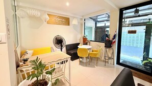 A modern living room with a sofa, yellow chairs, a dining table, a fan, and a potted plant. - Hostel 159 (Bangkok)