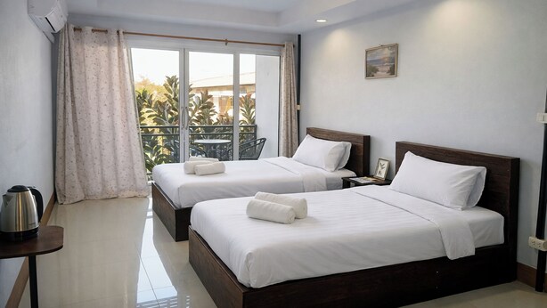 A hotel room with two beds, a small table with a kettle, and a view of a balcony with plants. - B&T Hostel (Chiang Rai)