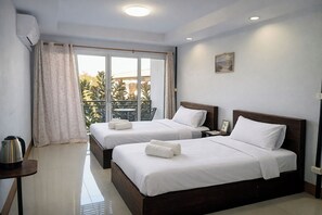A hotel room with two beds, a small table with a kettle, and a view of a balcony with plants. - B&T Hostel (Chiang Rai)
