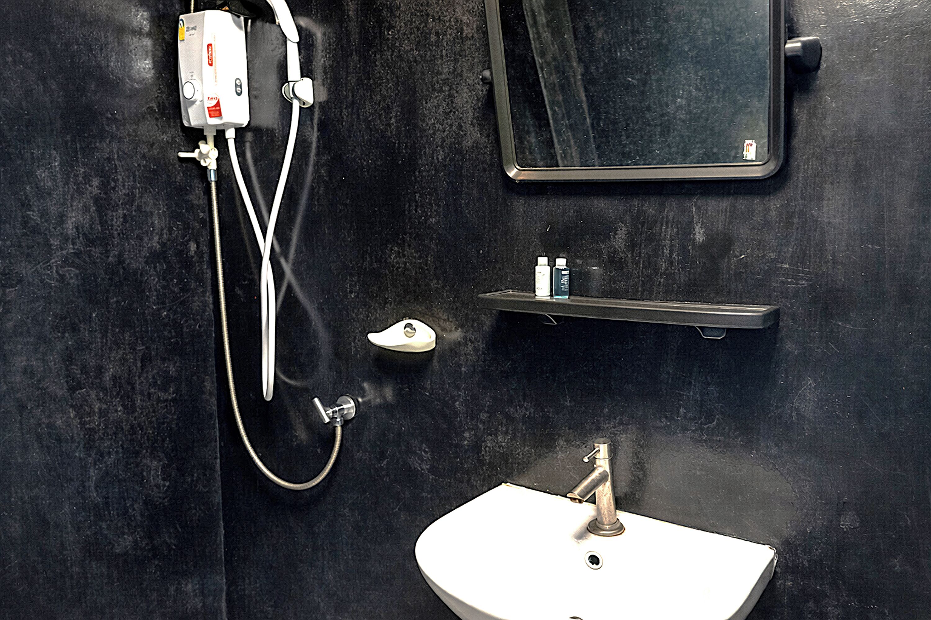 Un baño con lavamanos blanco, un espejo, cabezal de ducha y estante con artículos de aseo.