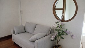 Un canapé gris avec des coussins, une plante orchidée en pot et un miroir rond accroché au mur.