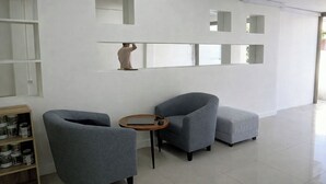 Une pièce moderne et minimaliste, avec deux fauteuils gris, une petite table en bois et une étagère ornée d’objets décoratifs.