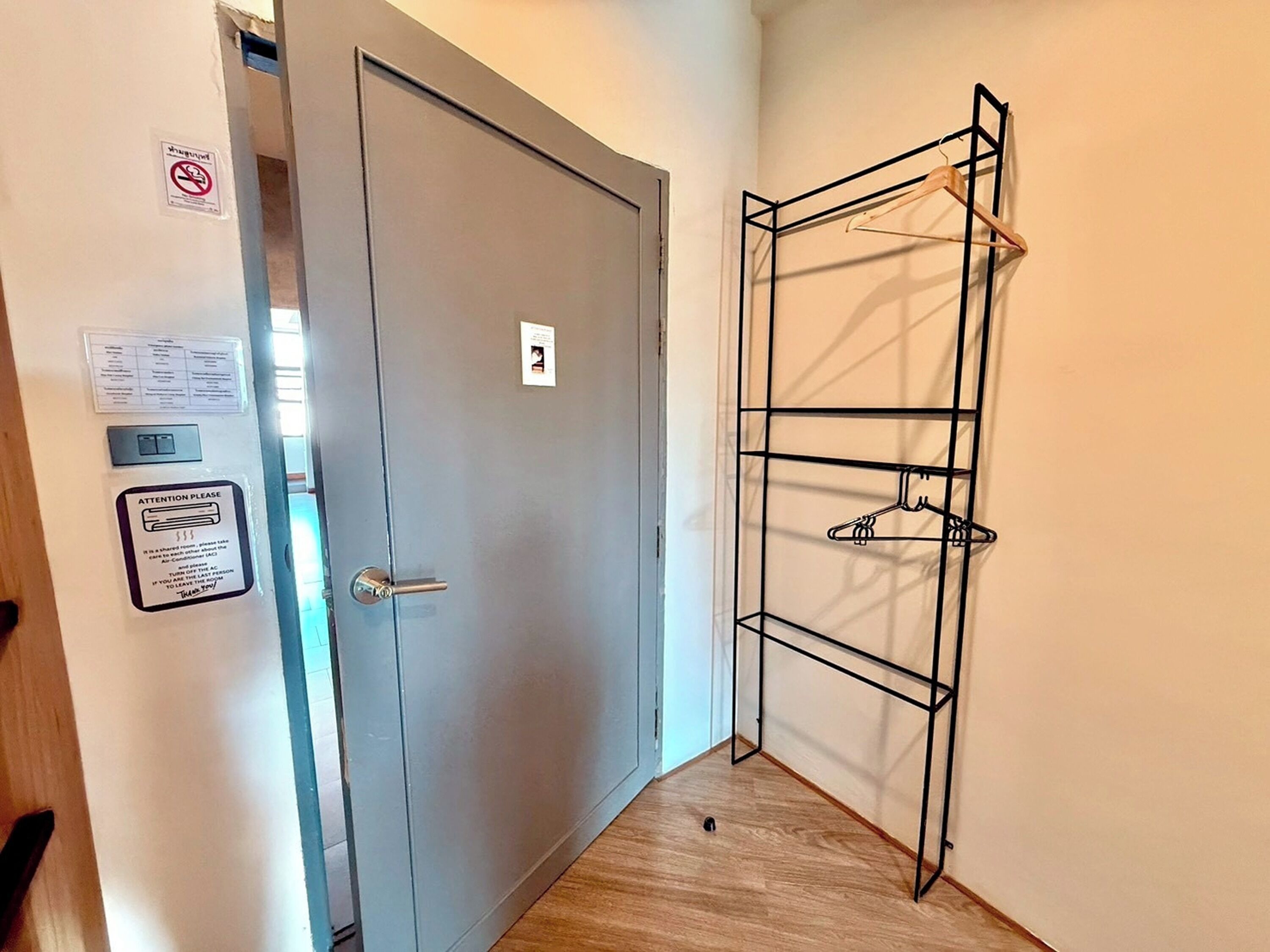 Un pasillo con una puerta gris, un perchero con ropa y un cartel de prohibido fumar.