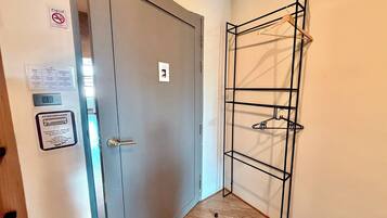 Un pasillo con una puerta gris, un perchero con ropa y un cartel de prohibido fumar.