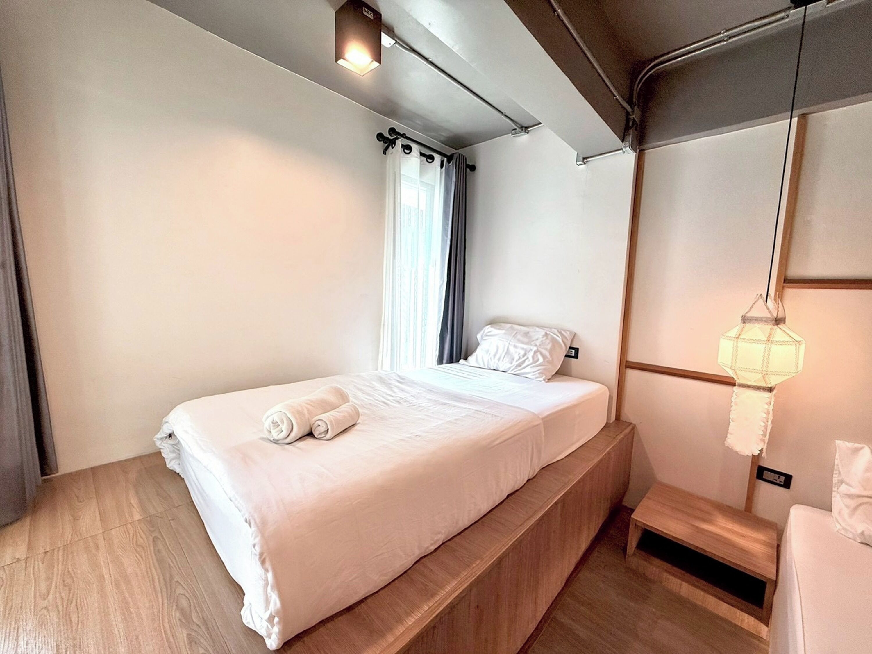 Een moderne hotelkamer met een eenpersoonsbed, nachtkastje, lamp en raam met gordijnen.