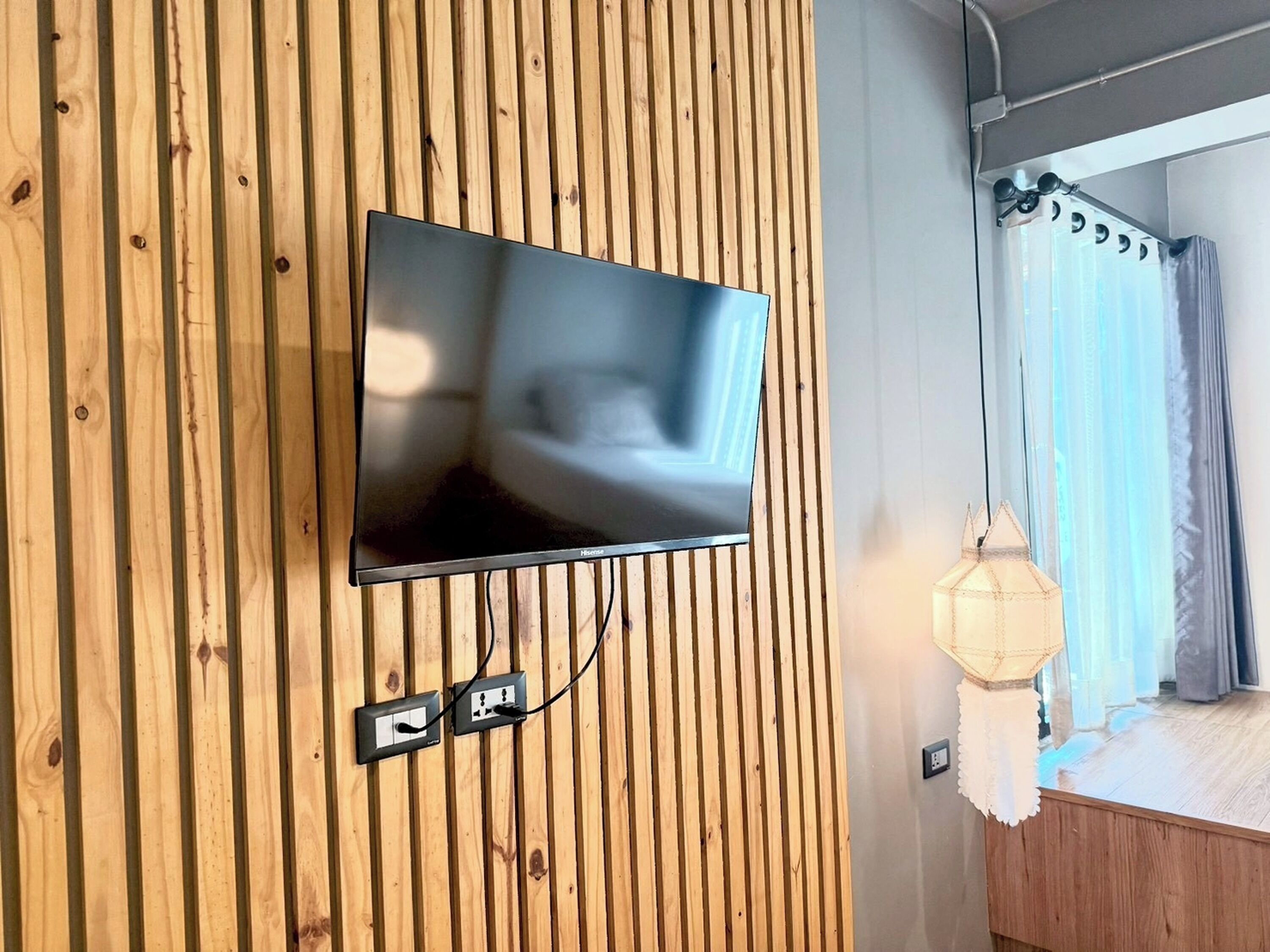 A television mounted on a wooden wall with a power outlet below it.